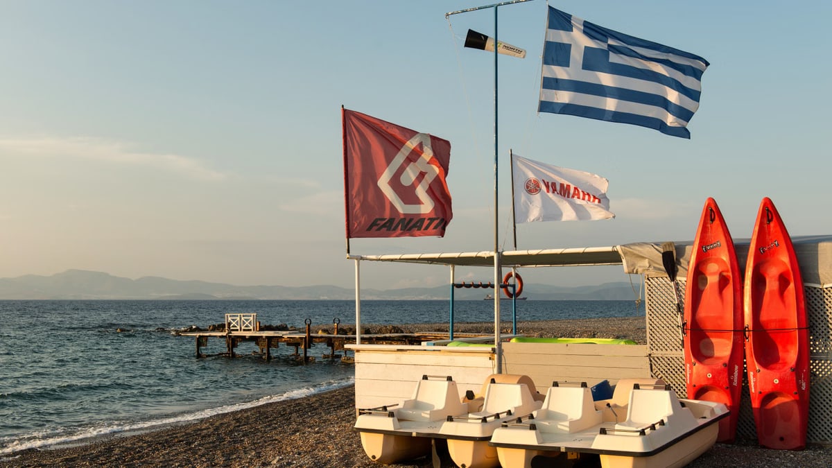 Tranquil beach scene on Kos island featuring paddle boats and Greek flags, ideal for tourism imagery.